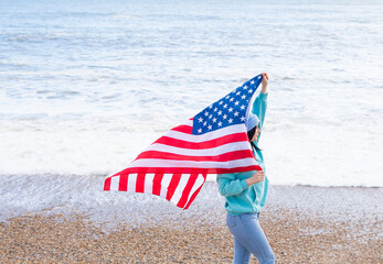 brunette woman in blue sweater and hat with american national flag near sea