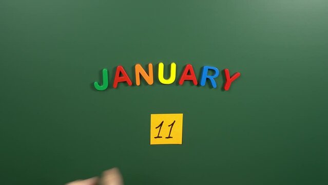 Hand sticking a sticker 11 January calendar day on school board. 11 date of January. Eleventh day of January. 11th date number. 11 day calendar. Eleven date