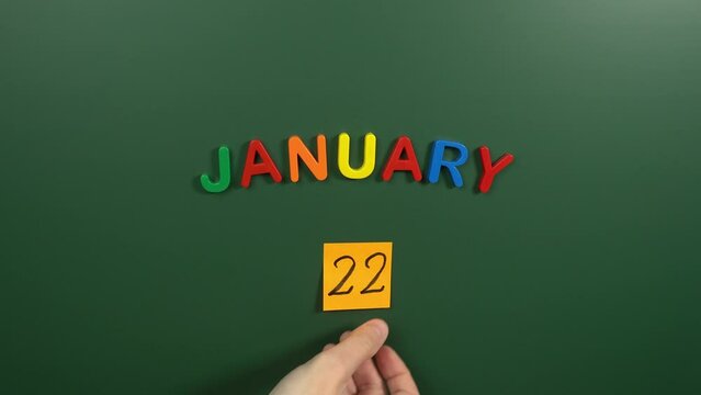 Hand sticking a sticker 22 January calendar day on school board. 22 date of January. Twenty second day of January. 22th date number. 22 day calendar. Twenty two date