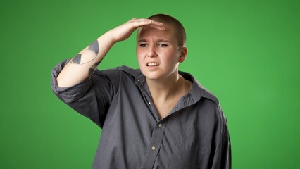 Portrait of happy smiling gender fluid non binary young woman 20s smiling and look around for friend find waving meet greet with hand as notices someone isolated on green screen background.