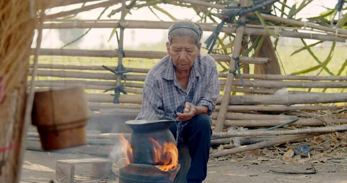 Asian rural life in the morning which is a poor farmer woman and employee in the farm, lighting fire for her breakfast cooking using a stove with firewood. There are smoke from firewood.
