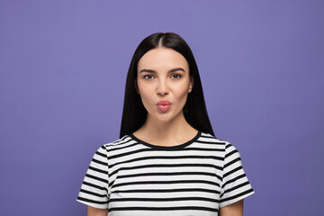 Fototapeta premium Beautiful young woman blowing kiss on purple background