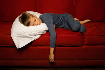 Youth child boy in pajamas laying on couch with pillow