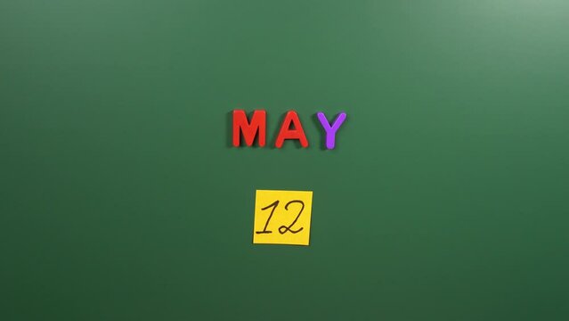 Hand sticking a sticker 12 May calendar day on school board. 12 date of May. Twelfth day of May. 12th date number. 12 day calendar. Twelve date. World Fibromyalgia Awareness