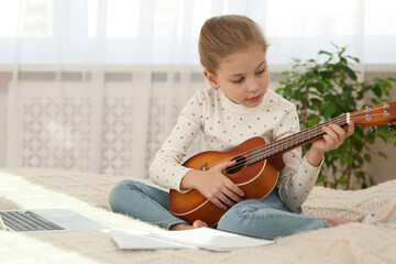Little girl learning to play ukulele with online music course at home. Space for text
