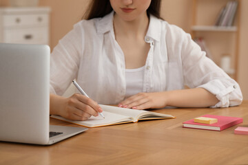 Woman writing in notebook at wooden table indoors, closeup