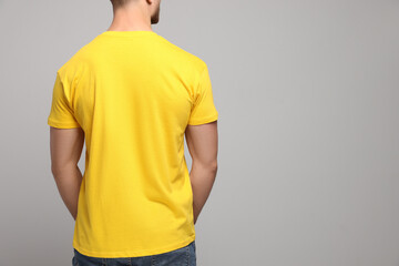 Man wearing yellow t-shirt on light grey background, back view. Mockup for design