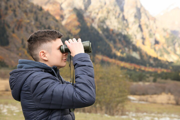 Boy looking through binoculars in beautiful mountains. Space for text