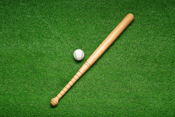Fototapeta na wymiar Wooden baseball bat and ball on green grass, flat lay. Sports equipment