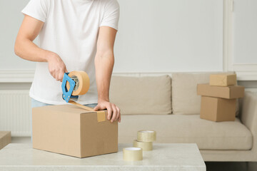 Fototapeta na wymiar Man packing box with adhesive tape indoors, closeup