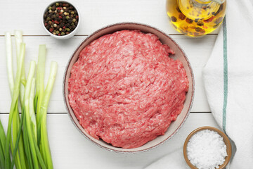 Bowl of raw fresh minced meat and ingredients on white wooden table, flat lay