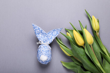 Easter bunny made of wrapping paper and egg near beautiful tulips on grey background, flat lay....