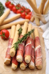 Delicious grissini sticks with prosciutto on white table