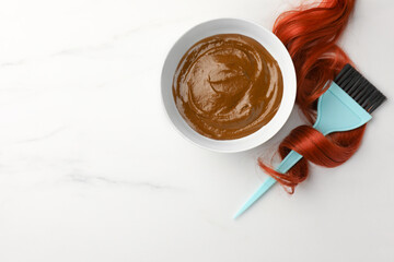 Bowl of henna cream, brush and red strand on white marble table, flat lay with space for text. Natural hair coloring