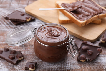 Jar with tasty paste and pieces of chocolate on wooden table