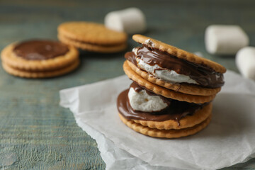 Delicious marshmallow sandwiches with crackers and chocolate on light blue wooden table, closeup. Space for text