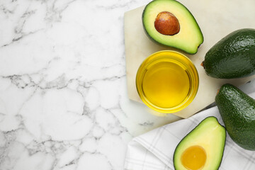 Bowl with oil and fresh avocados on white marble table, flat lay. Space for text