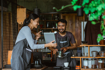 female barista showing the digital tablet at the male barista that brewing coffee inside the bar desk