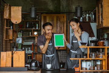shocked couple of barista closing their mouth with their hands while looking at the digital tablet with green screen