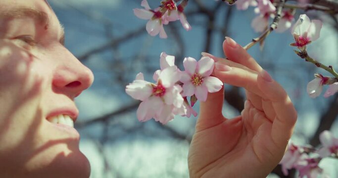 Lady smelling blossom flowers. Woman enjoying nature in spring apple orchard. Happy girl in garden with blooming trees.