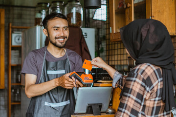 a female customer paying using the credit card at the coffee shop served by the male barista