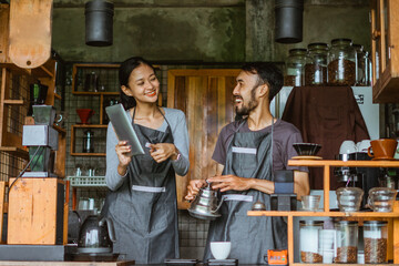 female barista smiling while pointing at the digital tablet and looking at the laughing male barista