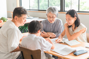 家のダイニングで孫の宿題を教える高齢者夫婦と小学生の子供
