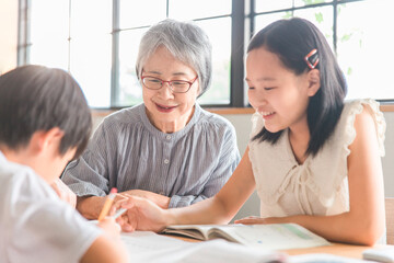 家のダイニングで孫の夏休みの宿題を教える高齢者女性と小学生の子供（帰省・里帰り）
