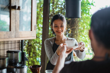 the male barista smiling while giving the cup of coffee to the female barista