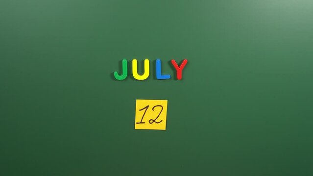 Hand sticking a sticker 12 July calendar day on school board. 12 date of July. Twelfth day of July. 12th date number. 12 day calendar. Twelve date. Malala, Paper Bag