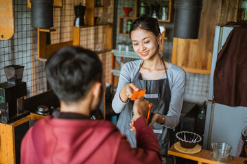 a beautiful barista receiving the credit card from the customer during the transaction on the cashier desk