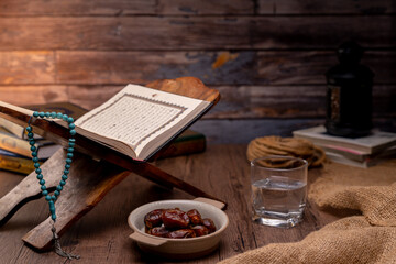 Many Date Palms are on bowls, plates, a cup of water, and the Quran, islamic style lamps on wooden tables, to wait for the time of Iftar, with the concept of ramadan Muslims around the world.