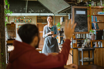 a customer calling the waitress that standing and holding the book of menu in front of the bar desk