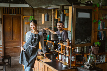 a female barista standing put her hand inside her pocket while the male barista standing inside the bar desk