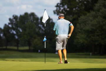 A male golfer walking towards a golf flag on the course with green grass underneath him.