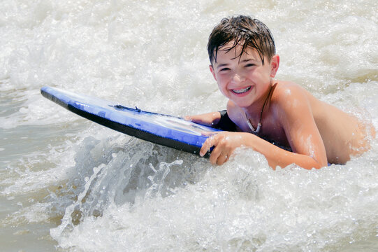 Happy young beach boy riding his boogie board in the surf