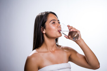 A beautiful young woman takes a moment to hydrate with water before going to bed. Shot in a studio on a white background, her natural beauty radiates.