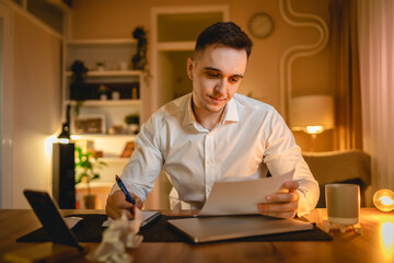 Fototapeta premium A young man is working late or studying at his home office while drinking coffee and using his mobile phone 