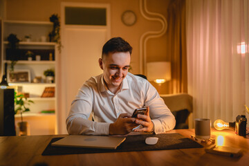 Obraz na płótnie Canvas A young man is working late or studying at his home office while drinking coffee and using his mobile phone 