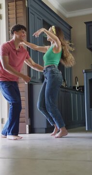 Vertical video of happy biracial couple spending time at home and dancing barefoot