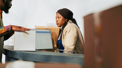 Depot worker planning stock logistics on computer, working with products in cardboard packages at...