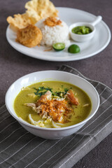 soto ayam or chicken yellow soup in white ceramic bowl, usually served with cooked rice, and potatoes cake