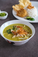 soto ayam or chicken yellow soup in white ceramic bowl, usually served with cooked rice, and potatoes cake