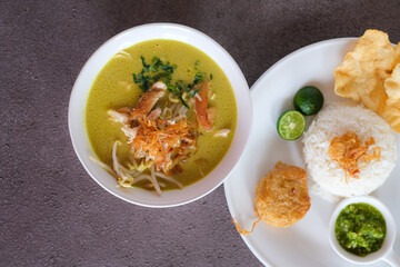 soto ayam or chicken yellow soup in white ceramic bowl, usually served with cooked rice, and potatoes cake