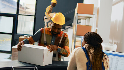 Young colleagues chatting about order shipment at work, planning manufacturing and stock production for retail store distribution. Team of warehouse employees working with merchandise. Handheld shot.