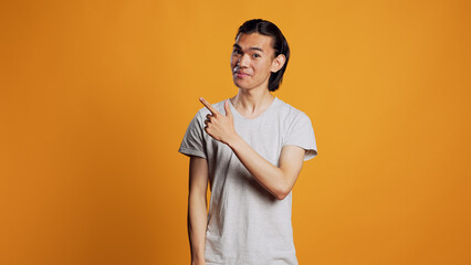Asian person pointing sideways with index fingers, looking left or right sides and being confident. Young male model indicating directions aside in studio, posing with confidence on camera.