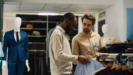 Obraz premium Young shopper asking shop worker for help with clothes, looking to buy formal wear from fashion boutique. Retail store assistant talking to customer about shopping for modern clothes.