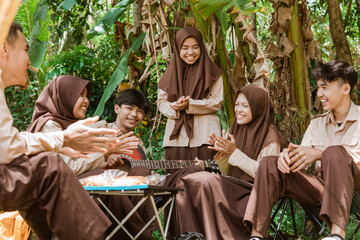 Boy Scouts and Girl Scouts singing clapping using a guitar against a natural background
