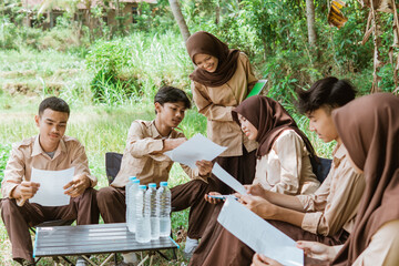 girl scout squad leader carrying tablet and her friends doing paper assignments during gathering