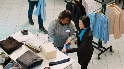 Group of diverse people examining trendy clothes in shop, checking discount on fashion collection....